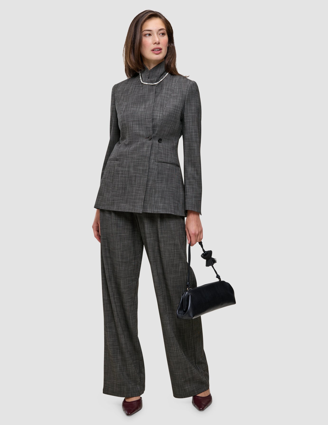 En kvinne i en kullgrå dress med en iøynefallende blazer og bukser, som holder en svart håndveske.